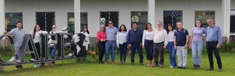 Hub colleagues smile and stand in a row on the grass, next to the Tecnicafe sign and in front of the white Tecnicafe building